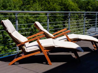 Deux chaises longues en bois confortables avec coussins blancs sur une terrasse avec vue sur des arbres verts.