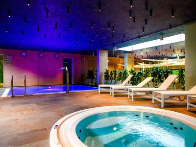 Espace bien-être moderne avec jacuzzi, piscine et chaises longues sous un éclairage d'ambiance.