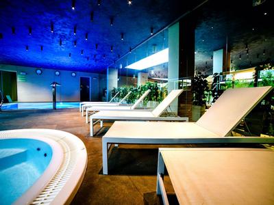 Espace intérieur d'un hôtel avec plusieurs chaises longues à côté d'un jacuzzi sous un éclairage bleu.