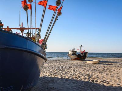 Deux bateaux de pêche sur une plage de sable avec un ciel bleu clair et une mer calme en arrière-plan.