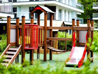 Une aire de jeux en bois colorée avec toboggan et structures d'escalade devant un bâtiment résidentiel moderne.