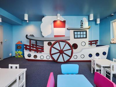 Salle de jeux pour enfants avec un bateau mural et des meubles colorés dans un hôtel.