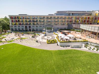 Complesso alberghiero moderno con balconi su più piani e giardino curato sotto un cielo azzurro.