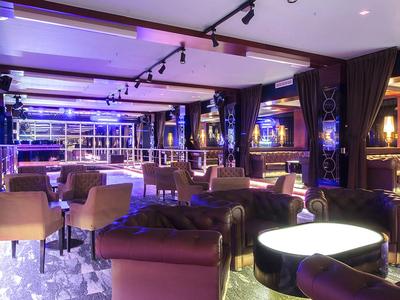 Area bar moderna di un hotel con sedie eleganti, bancone illuminato e atmosfera soffusa.