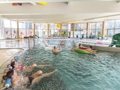 Area piscina interna con diverse persone che nuotano e si rilassano su ciambelle gonfiabili.