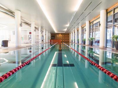 Area piscina interna moderna con corsia di nuoto, grandi finestre e piante decorative.