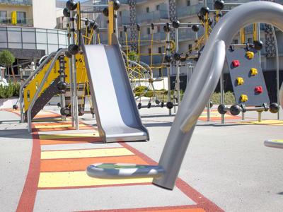 Parco giochi moderno con struttura da arrampicata e scivolo in cortile di un hotel alla luce del giorno.