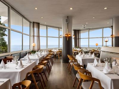 Modernes Restaurant mit großen Fenstern und gedeckten Tischen mit Blick auf die Landschaft.