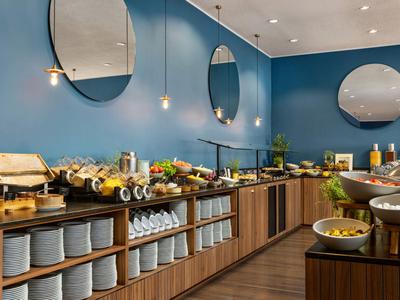 Hotelbuffet mit vielfältigen Speisen, hölzernen Regalen und blauen Wänden mit runden Spiegeln.