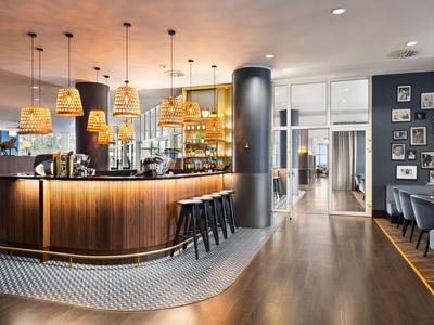 Moderne Hotelbar mit Holztheke, Hockern, Lampen und gemütlichem Sitzbereich.