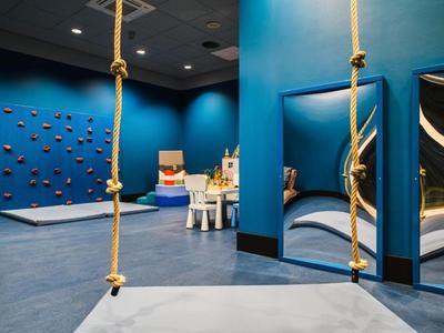 Moderner Indoor-Spielbereich mit blauem Kletterwand, Schaukeln und Sitzgelegenheiten.