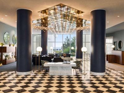 Großer Hotel-Lobbybereich mit schwarzem und weißem Schachbrettboden, Säulen und modernen Möbeln.