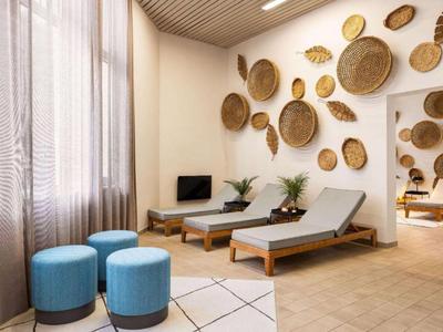 Helles Spa-Wartezimmer mit zwei Liegen, blauen Hockern und Wanddeko aus Flechtkörben.