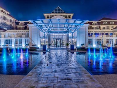 Hotel moderno de noche con entrada iluminada en azul y fuentes de agua.