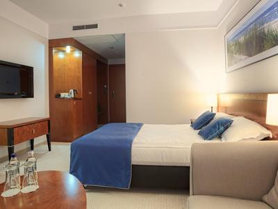 Habitación de hotel moderna con cama doble, colcha azul y televisor en la pared.