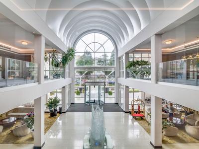 Átrio luminoso de hotel con techo de vidrio, plantas y áreas modernas de descanso a ambos lados.