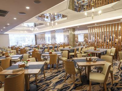 Gran comedor de hotel con numerosas mesas, sillas y luces modernas en el techo.