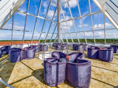 Zona de lounge con sillas moradas dentro de una sala piramidal de vidrio con vista al paisaje.