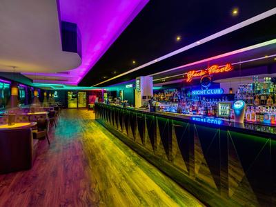Área de bar de hotel moderna con iluminación LED colorida y mostrador largo.