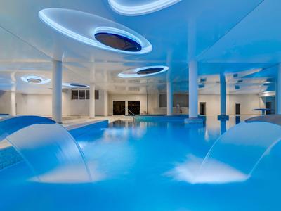 Moderna zona de piscina cubierta con chorros de agua y luces de techo futuristas.