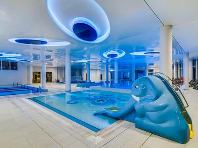 Piscina cubierta luminosa con tobogán y luces azules en el techo.