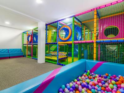 Parque infantil interior colorido con estructura para escalar y piscina de bolas en una habitación luminosa.