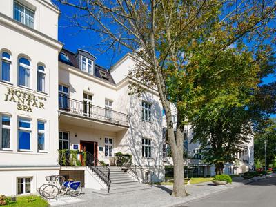 Historisches Hotelgebäude mit weißer Fassade, Eingangsbereich mit Treppen und Bäumen entlang des Gehwegs.
