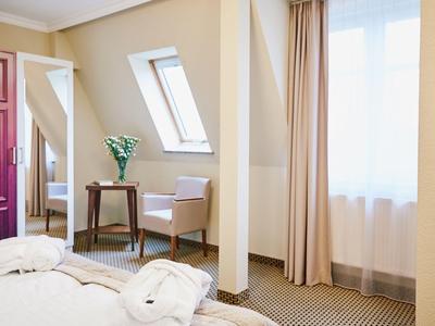 Helles Hotelzimmer mit einem Bett, einem Stuhl, einem kleinen Tisch und Fenstern mit Vorhängen.