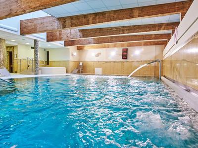 Innenpool mit Holzdecke, Wasserfontänen und bequemen Liegen in einem Hotel-Spa-Bereich.