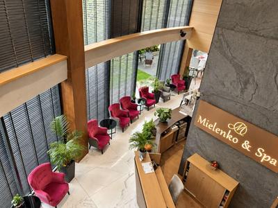 Moderne Hotellobby mit roten Sesseln, Pflanzen und einem Empfangstresen.