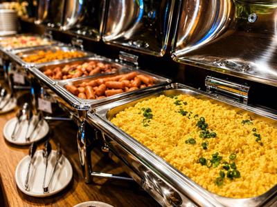 Buffet mit verschiedenen warmen Speisen in glänzenden Edelstahlbehältern an Holztisch.