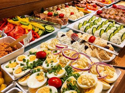 Vielfältiges Frühstücksbuffet mit Eiern, Gurken, Tomaten und Aufschnitt in Holzambiente.