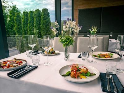 Elegantes Restaurant mit weißen Tischtüchern, Blumen und angerichteten Speisen am Fenster mit Aussicht.