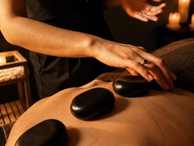 Drei heiße Steine liegen auf dem Rücken einer Person bei einer Massage im gedämpften Licht.