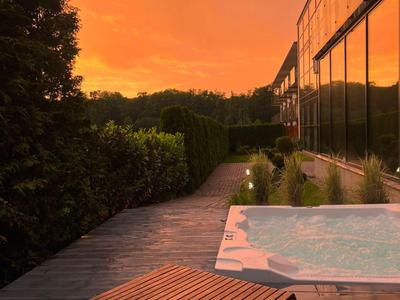 Abendstimmung mit Holzliege und beleuchtetem Pool an einem Hotelgarten.