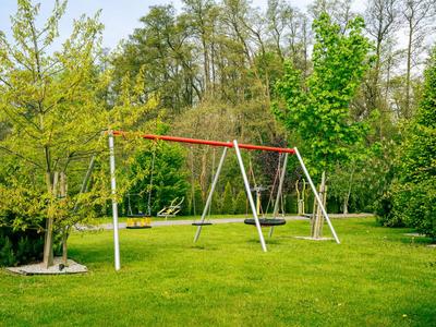 Leerer Kinderschaukelrahmen auf grünem Rasen vor Bäumen im Garten eines Hotels.