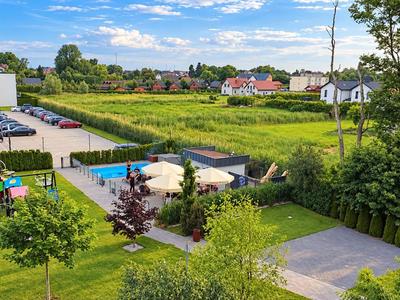 Außenbereich eines Hotels mit Garten, Sitzbereich, Parkplatz und Blick auf grüne Felder und Häuser.