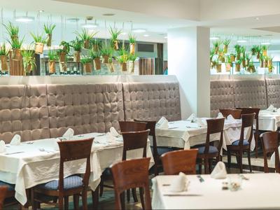 Stilvolles Restaurant mit weißen Tischdecken, hölzernen Stühlen und vielen Pflanzen als Dekoration.