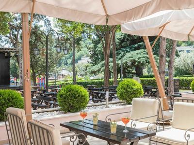 Terrassenbereich eines Cafés mit Tischen, Stühlen und Sonnenschirmen im Grünen