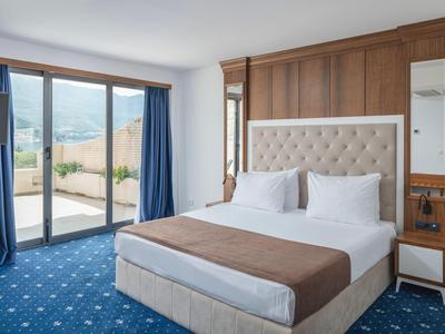Gemütliches Hotelzimmer mit Doppelbett, Holzwand, blauen Vorhängen und Balkon mit Bergblick.