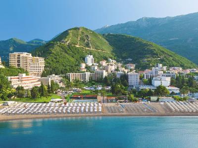 Strand mit Sonnenschirmen vor einem Ort mit grünen Hügeln und Bergen im Hintergrund