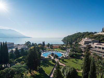 Hotelanlage mit Pool, Gärten und Blick auf das Meer und Berge bei klarem Himmel.