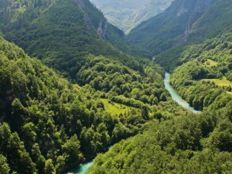 La rivière serpente à travers une vallée verdoyante et boisée entre de hautes montagnes sous un ciel nuageux.