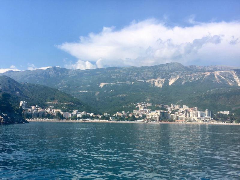 Vue d'une ville côtière avec des montagnes en arrière-plan et une eau calme au premier plan.