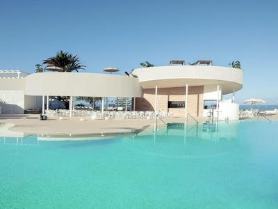 Moderner Pool mit klarem Wasser und weißem, rundem Gebäude im Hintergrund unter blauem Himmel.