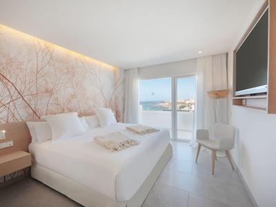 Helles Schlafzimmer mit großem Bett, zarten Wandmustern, Balkon und modernem TV an der Wand.