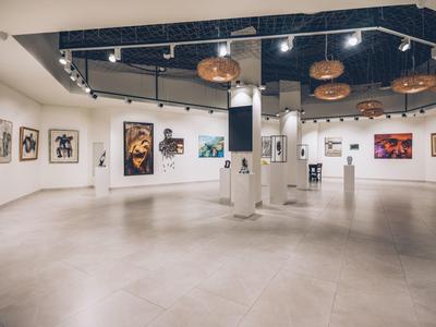 Großer, heller Ausstellungsraum mit weißen Wänden, farbigen Gemälden und moderner Beleuchtung.