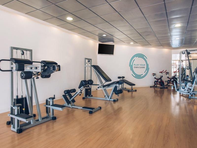 Moderne fitnessruimte met verschillende trainingsapparaten en houten vloer in een hotel.