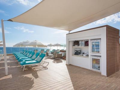 Sunny rooftop terrace with lounge chairs and small kiosk by the sea.