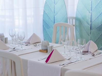Elegant set table with white chairs and blue leaf decorations in the background.